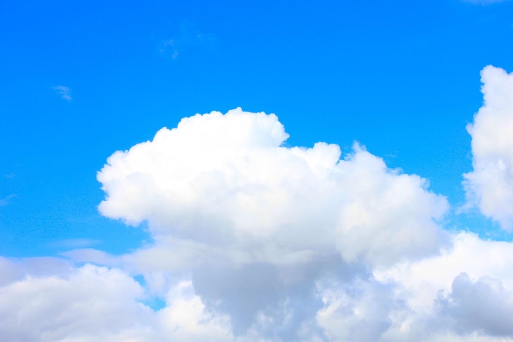 A wide blue sky holds a soft, bright cloud drifting gently above a layer of lighter mist, glowing in the midday light.