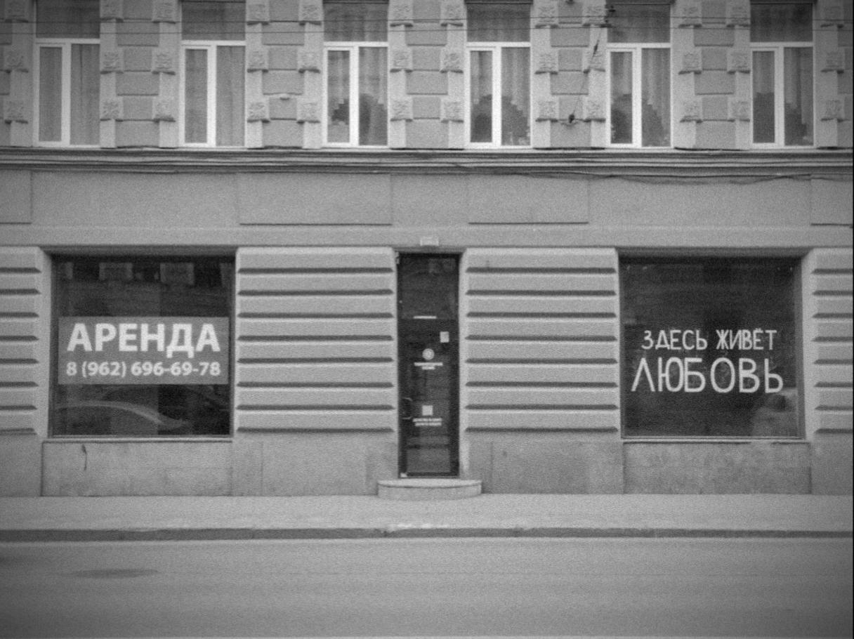 Чёрно-белое фото витрины в старом здании. Надпись в правом окне: «Здесь живёт любовь». Надпись в левом окне: «Аренда».

B&W photo of a two shop windows. On the right window: "Here lives the love". On the left window: "Available for rent"