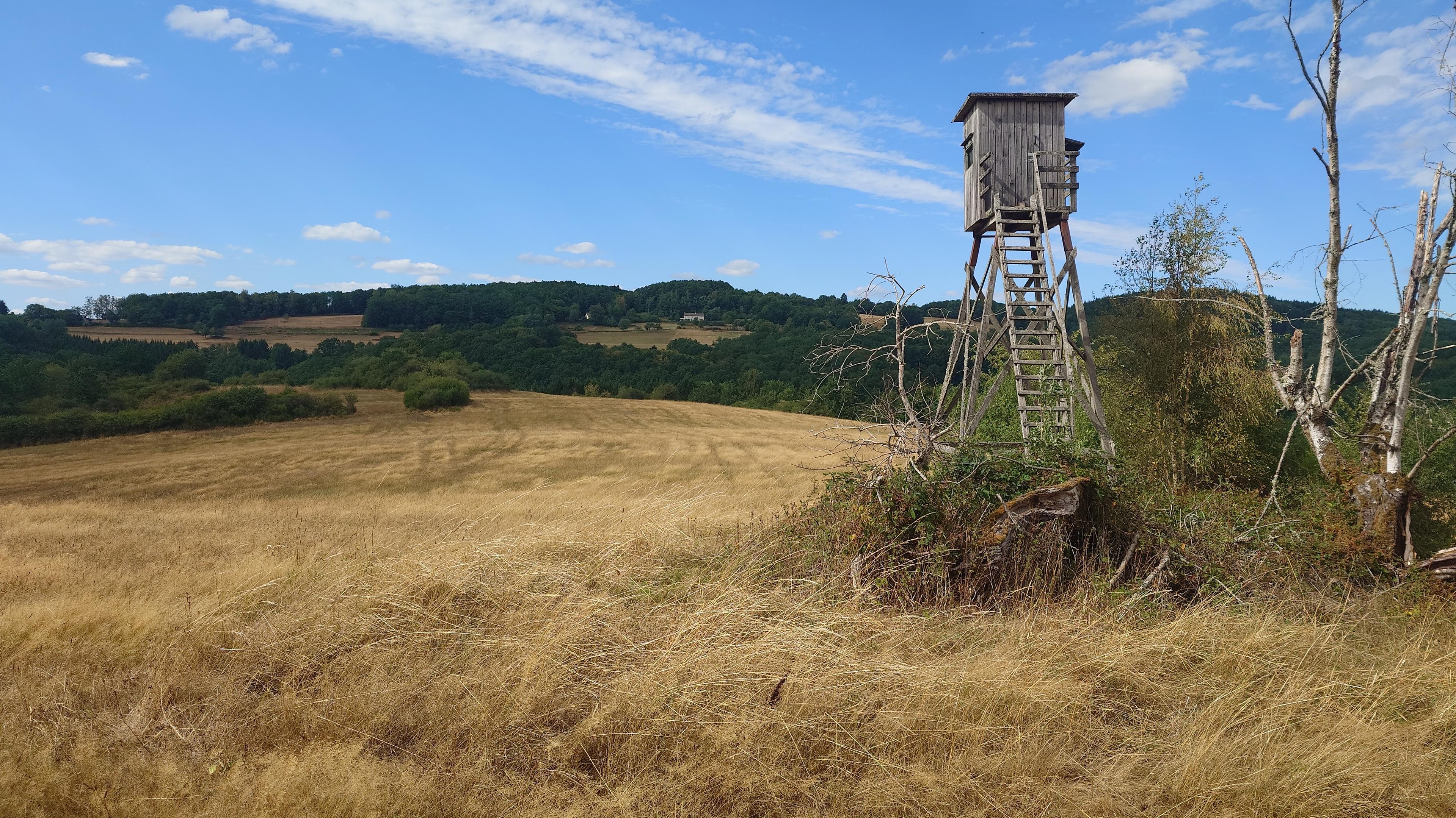 Lonely watchtower on a dry-grass covered hill. The sky is clear with just a couple of white fluffy cloud patches, more green hills visible in the distance.